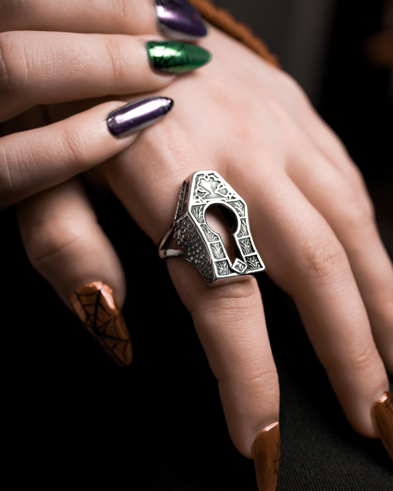 Model wearing large gravestone shaped stainless steel ring with filigree detailing and a keyhole detail in the middle. Shown from a left side angle