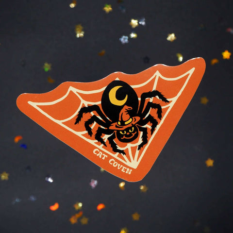 die-cut vinyl sticker with orange background picturing black spider with orange witch hat and yellow crescent moon on its thorax on a white triangular shaped white web