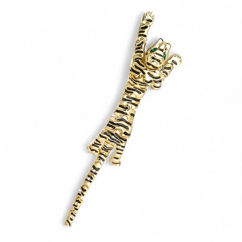 Gold tiger brooch with articulated body and jeweled green eyes on a white background