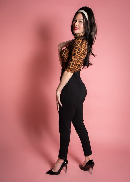 model wearing a pair of black knit cigarette style pants with a high waistband and vertical darting. Shown from the side on a pink background.