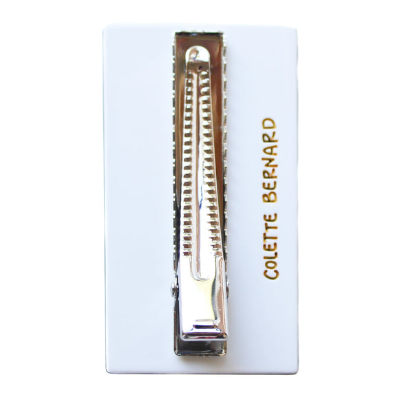 Rectangular white bioacetate hair clip in the shape of a doctor's eye chart with black letters in rows that get progressively smaller. Shown from back to display alligator style clip and gold branding
