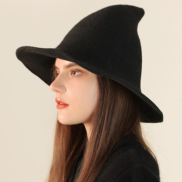 Woman wearing a black textured ribbed knit witch hat against a plain background. Shown from side