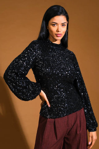 model wearing a black top with high neckline and long balloon-style sleeves in an allover black sequin fabric. Shown from front
