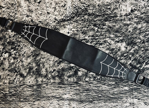 black faux leather wide wrap belt with black ribbon ties and white printed image of spiderweb corners at each end of the belt. Shown flat