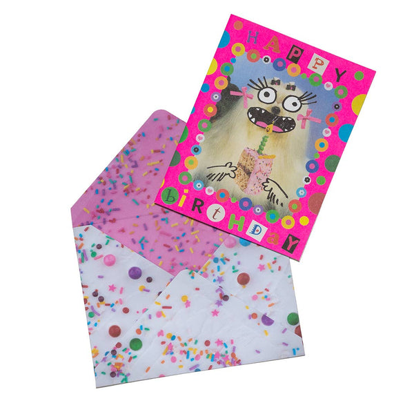 "Happy Birthday" message collage card with neon pink background & polka dots with photo of Maltese dog with added cartoon face blowing out the candle on a slice of birthday cake. Shown with frosting and sprinkles patterned envelope