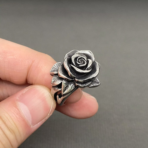 silver stainless steel ring in the shape of a blossoming camellia flower and its leaves. Shown held to display leaf detail
