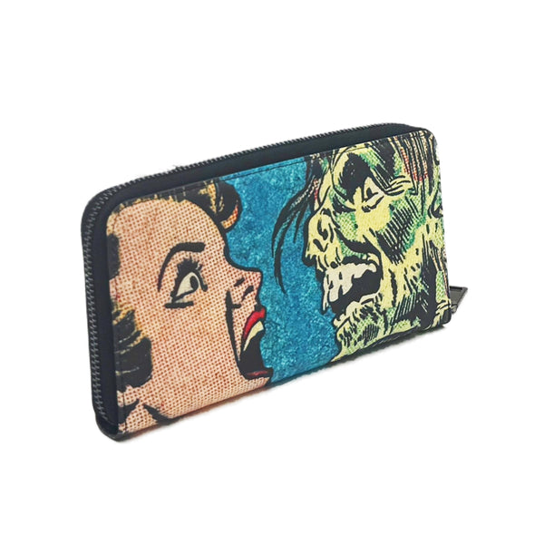 faux leather wristlet wallet with a printed Ben-Day woman's face and green monster design on a blue background shown from three quarter angle to display zip closure