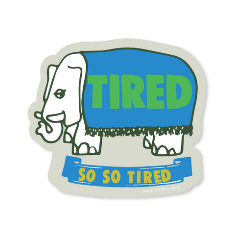 die-cut matte finish vinyl sticker of white elephant wearing a blue blanket reading "TIRED" in green letters with ribbon underneath reading "SO SO TIRED"