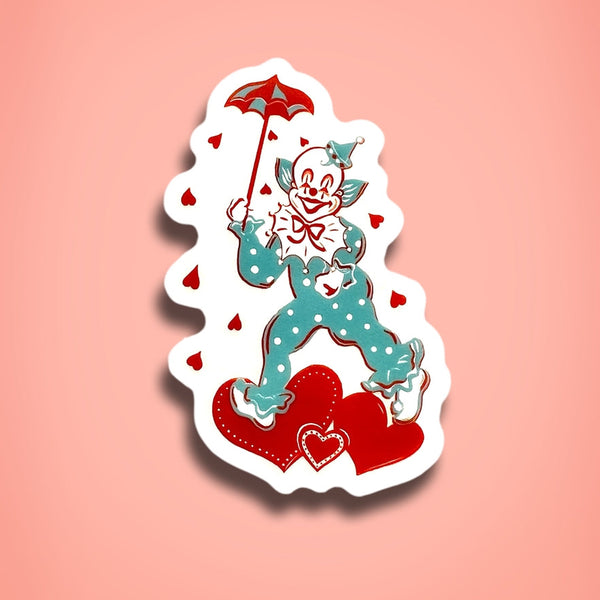 Transparent sticker of a clown with a white and teal polka dot outfit holding a red umbrella and surrounded by hearts shown on a pink background