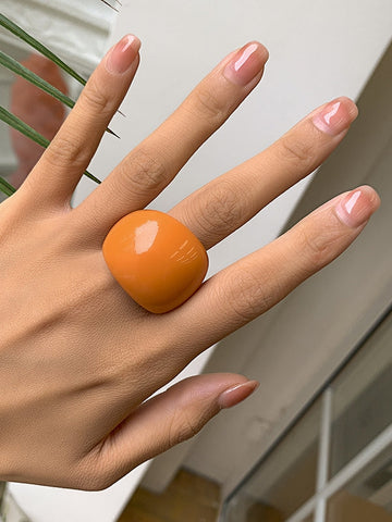 Rounded acrylic cocktail ring in bright orange. Worn by a model