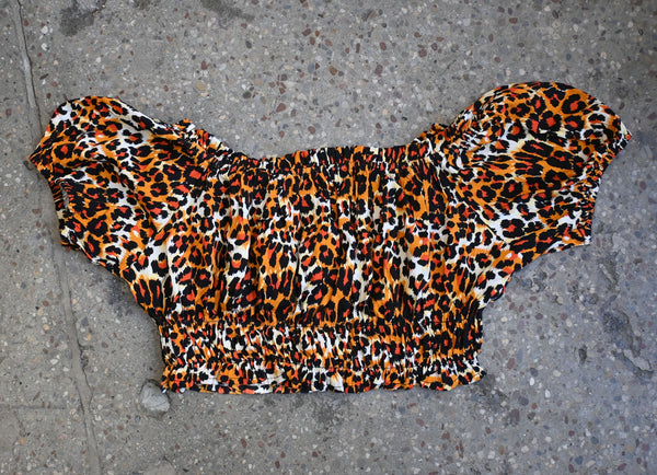 Orange, white, and black leopard print patterned rayon crop peasant blouse style top with wide rounded neckline, cap sleeves, and elasticized hemming at neckline, sleeves, and bottom hem. Shown from front lying flat