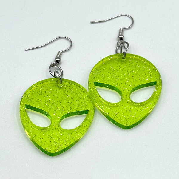 Neon green transparent acrylic with silver glitter alien head-shaped dangle earrings shown flat on white background