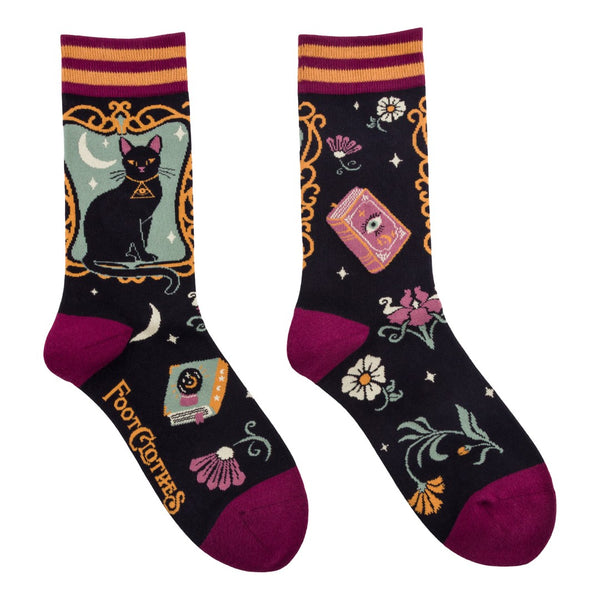 Cotton blend unisex crew socks with framed illustration of black cat on mint green background with black background pattern of flowers, stars, moons, and spell books. Socks have maroon toes and heels & maroon and golden yellow striped cuffs. Shown flat