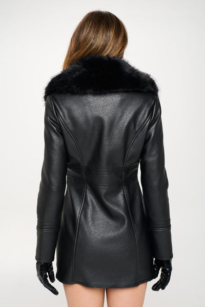 model wearing black faux leather fingertip length coat with oversized black faux fur shawl collar and side seam pockets. Shown from back zipped up