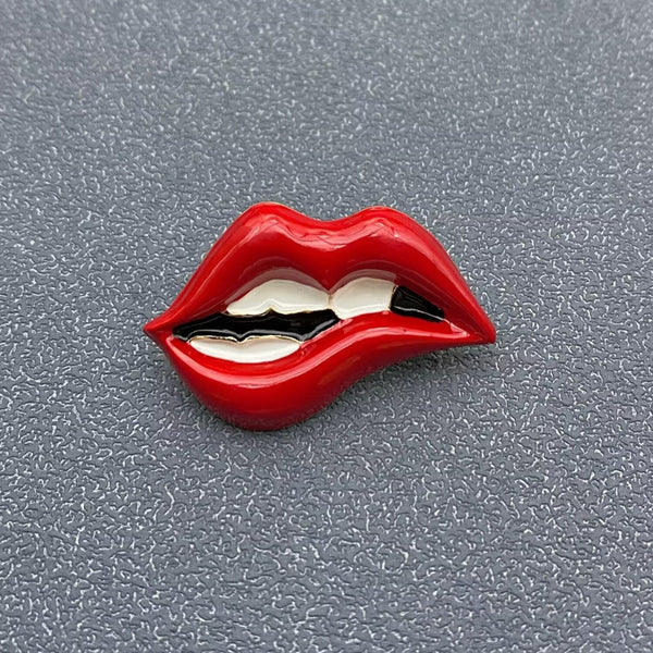 gold metal brooch of mouth with red enameled lips and white teeth in bottom lip biting pose. Shown from front