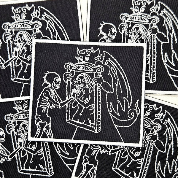 embroidered black twill patch with white border featuring white woodcut-style art of a devil holding a mirror to a skeleton and showing them the reflection of a woman. Shown flat with multiple patches