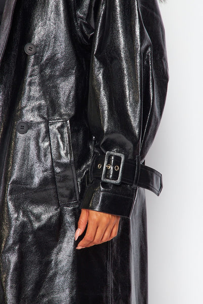 model wearing oversized shiny textured pvc black trench coat with notched collar, relaxed shoulders, self belt with self buckle and oversized buckles at cuffs, double breasted button closure, and slash pockets. Shown from side with coat open in close up