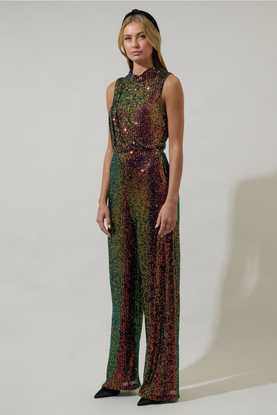 model wearing an iridescent sequin jumpsuit with shades of green, yellow, orange, and purple. Jumpsuit is sleeveless, has a mock neck, asymmetrical draped bodice detail and wide leg pants. Shown from side