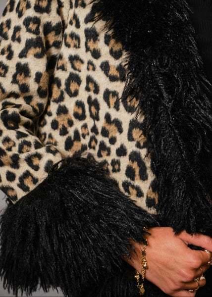Woman wearing a leopard print coat with a black shaggy fur collar, cuffs, and bottom hem against a gray background. Shown from front in close up of collar and print