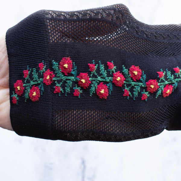 Black cotton socks with a knit-in pattern of red and green flowers and panels of patterned mesh. Shown stretched to show mesh detail