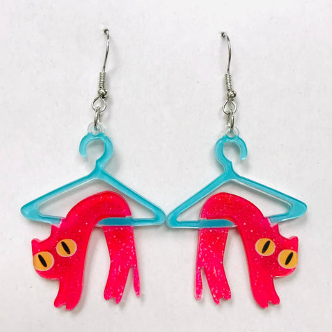 Dangle earrings made of laser-cut acrylic with printed image of pink cat designs on blue hangers against a white background
