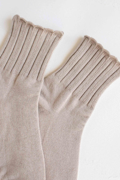 Light beige cotton knit socks with ribbed pattern and scalloped cuffs. Shown flat in close up