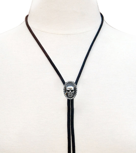 Silver metal skull pendant bolo tie with black rayon cord and silver metal tips. Shown on a dress form in close up