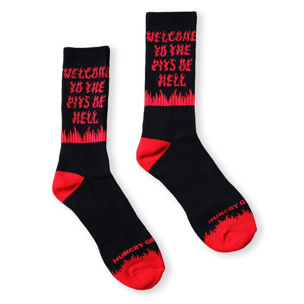 A pair of black unisex cotton crew socks with red flame accents and bold red text reading "WELCOME TO THE PITS OF HELL" and red heels and toes with "HUNGRY GHOST PRESS" writing. Shown from side