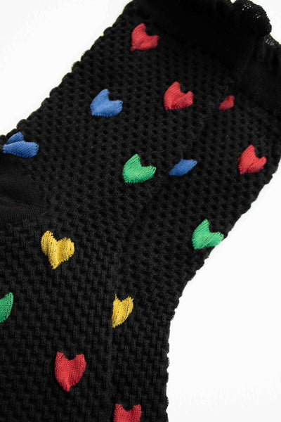 black cotton socks with waffle texture knit, ruffled cuffs, and knit-in pattern of red, blue, green, and yellow hearts. Shown in close up