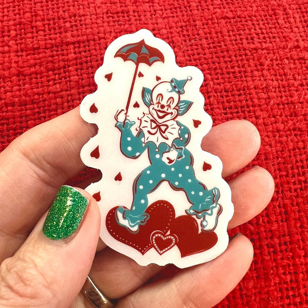 Transparent sticker of a clown with a white and teal polka dot outfit holding a red umbrella and surrounded by hearts shown on a pink background Transparent sticker of a clown with a white and teal polka dot outfit holding a red umbrella and surrounded by hearts shown held against a red background