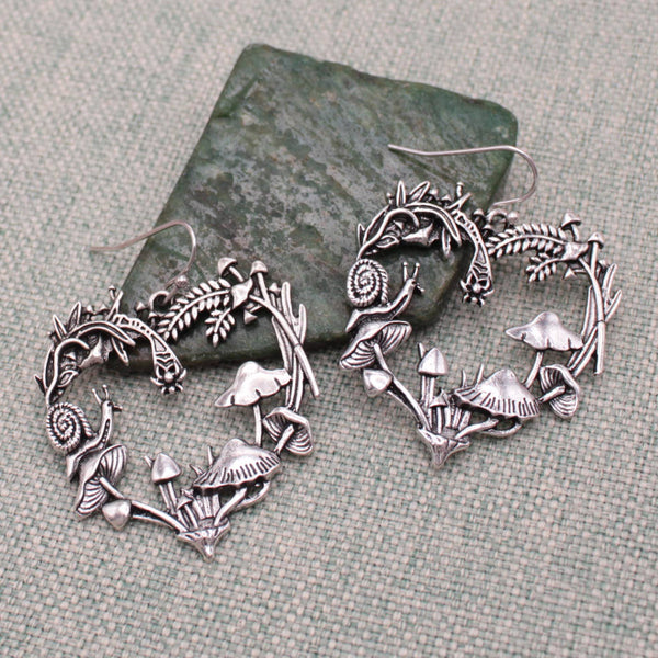 silver metal dangle earrings with charms in the shape of hearts made of mushrooms, snails, and leaves