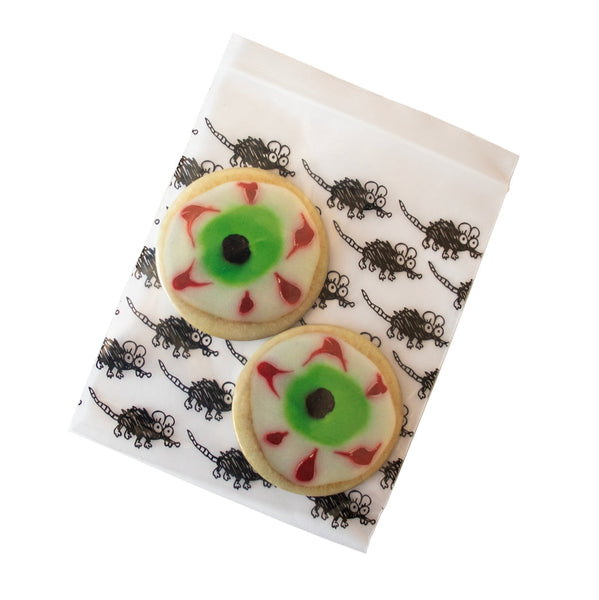 2 1/2" round magnet set of two magnets in the shape of sugar cookies with green, red, black and white eyeball frosting decoration. Shown in cartoon rat plastic bag packaging