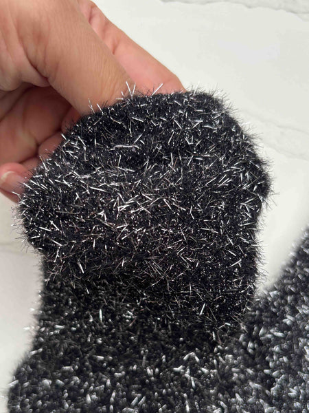 a pair of fuzzy knit crew length socks in black with long strands of silver lurex woven in and sticking out. Shown flat on white background in close up held by hand to display texture of knit fabric