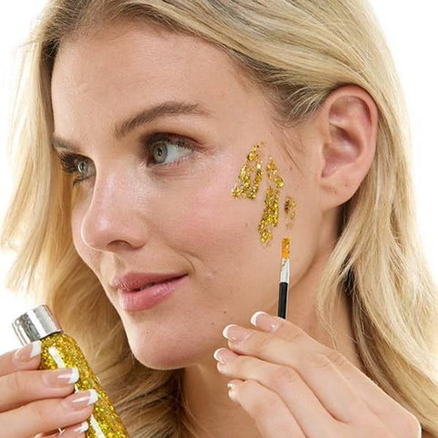 Woman applying gold decorative glitter makeup with a brush on a white background