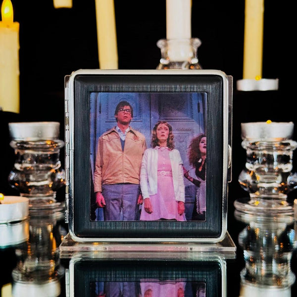 square metal cigarette case with lenticular image of Brad, Janet, and Magenta from the Rocky Horror Picture Show on front of case. Shown closed