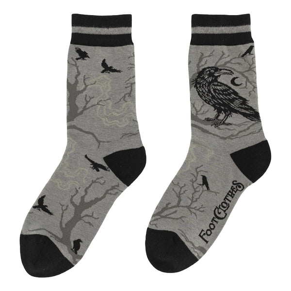 pair of medium grey cotton blend crew socks with solid black toes and heels & striped black and grey cuffs. All over pattern of a large crow on the outer ankle with a tree in the background with crescent moons and small flying crows in black. Shown flat from opposite side