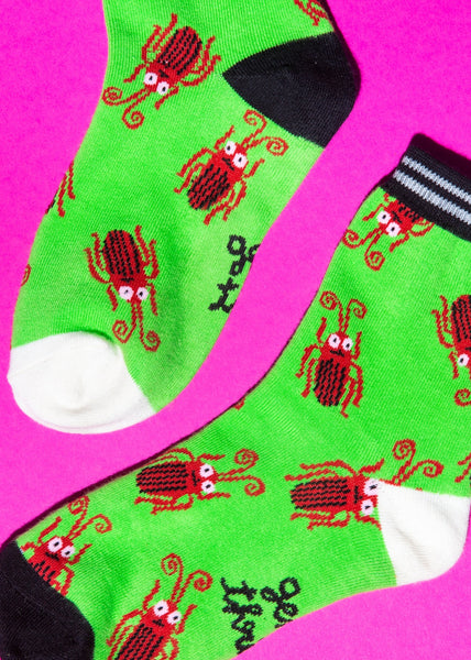 lime green crew socks with black and white striped cuffs and alternating black and white heels and toes, with an all-over pattern of brown cockroaches. Shown in close up on neon pink background