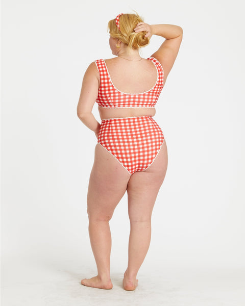 model wearing red and white gingham print reversible bikini. Top has scoop neckline and white rickrack style trim. Shown from back with gingham side worn