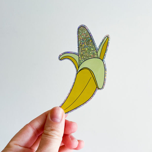 die-cut holographic sticker of a half peeled banana. Shown held in front of a white background