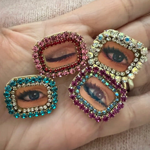 rectangular brooches with lenticular winking eye design and colorful rhinestones borders, shown held in a hand