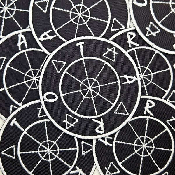 round black twill embroidered patch with white design of tarot wheel of fortune, element symbols, and letters spelling 'TAROT'. Shown flat with multiple patches