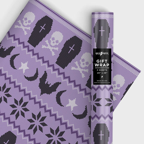 a roll of matte finish gift wrap in an all-over  Fair Isle style sweater pattern with a purple background and black & white coffins, skulls, moons, stars, and bats. Shown in a roll and flat