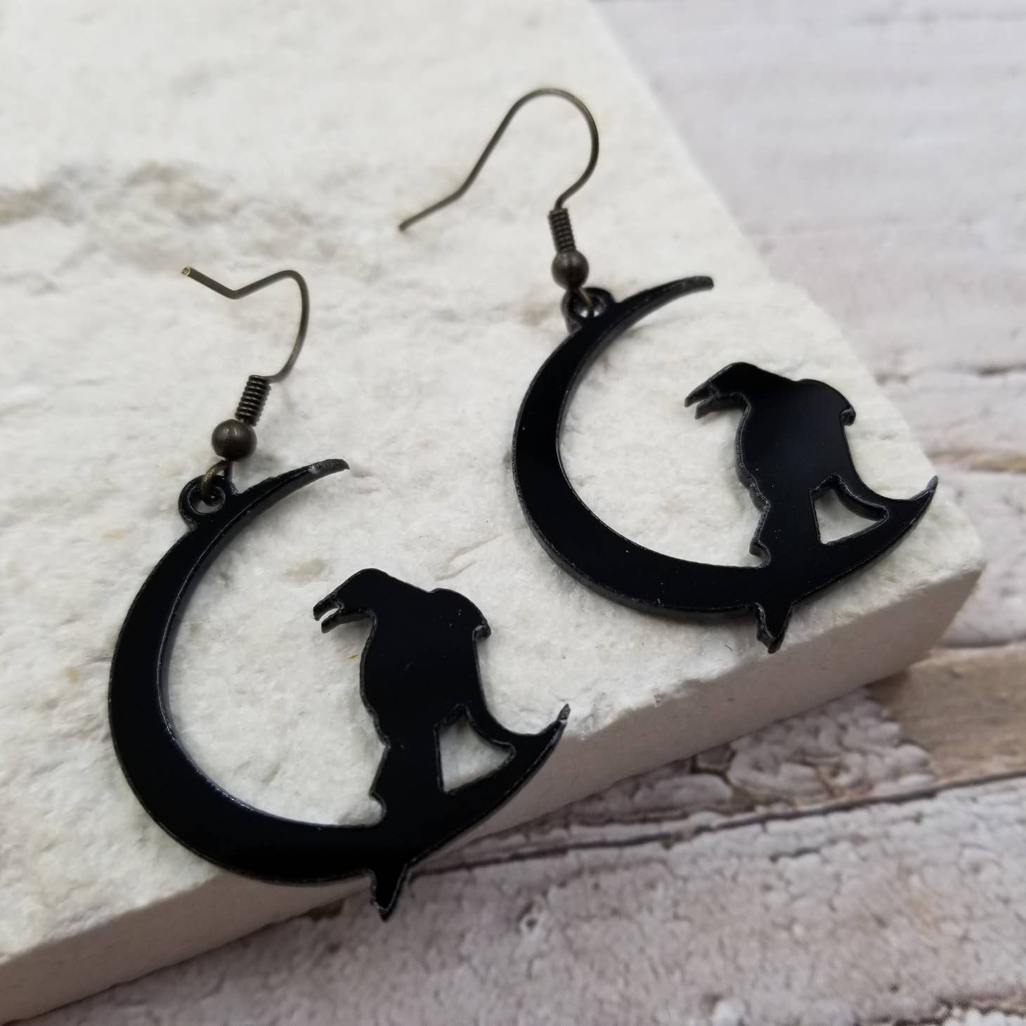 Laser cut acrylic dangle earrings in the shape of a crow perched on a crescent moon. Shown laying flat