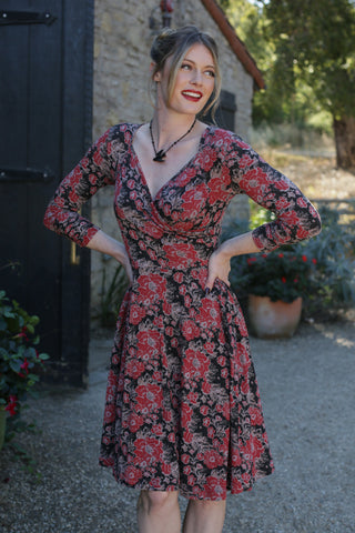 model wearing a black, red, and tan floral print 3/4 sleeve fit and flare dress in an outdoor setting