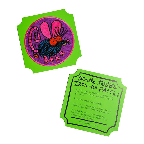 round embroidered patch with purple background and pink border of black and blue cartoon rat with big pink ears, red eyes, a curly tail with red purse hanging from it, and long red pointy nails. Shown on green backing card with iron-on instructions