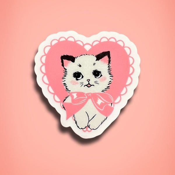 Transparent sticker of a cat with a pink bow on a heart-shaped border against a pink background