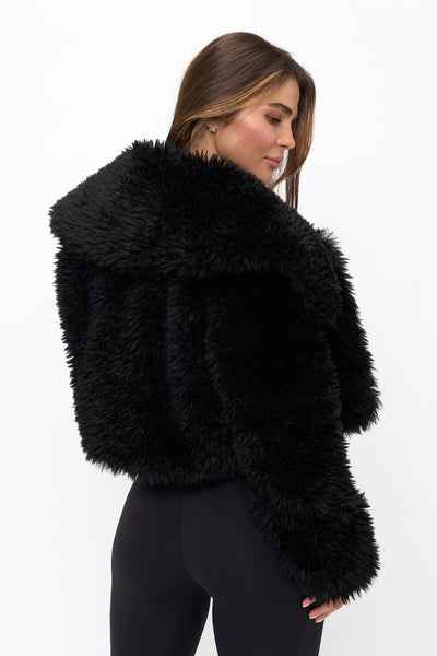 model wearing a black faux fur fluffy cropped jacket with oversized round collar. Shown from back