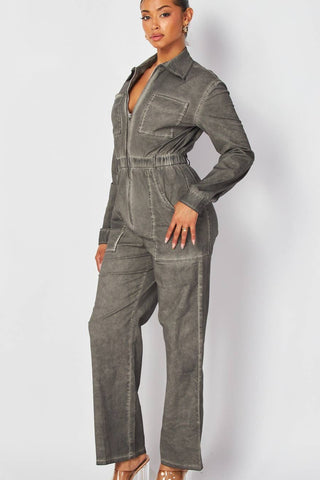 model wearing denim boilersuit in grey mineral wash finish. Boilersuit has long sleeves, pointed collar, silver metal zip down the center, elasticized waist with belt loops, large hip pockets and chest pockets, and full length legs. Shown from three quarter angle