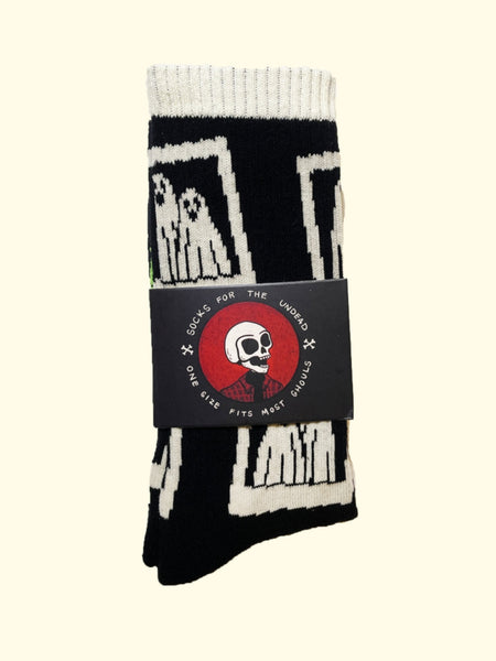 black cotton unisex crew socks with an all-over print of instant film camera pictures of a pair of ghosts wearing sheets. Shown in packaging