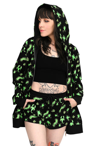 model wearing a black long sleeve hooded sweatshirt with neon green insect pattern, front silver metal zip closure, and patch pockets. Shown from front unzipped with hood up